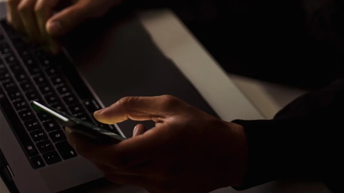 Person holding a smartphone while working on a laptop